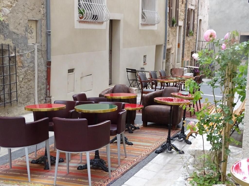 Un espace café en plein air avec des tables et des chaises rondes, un tapis à motifs et une plante en pot.