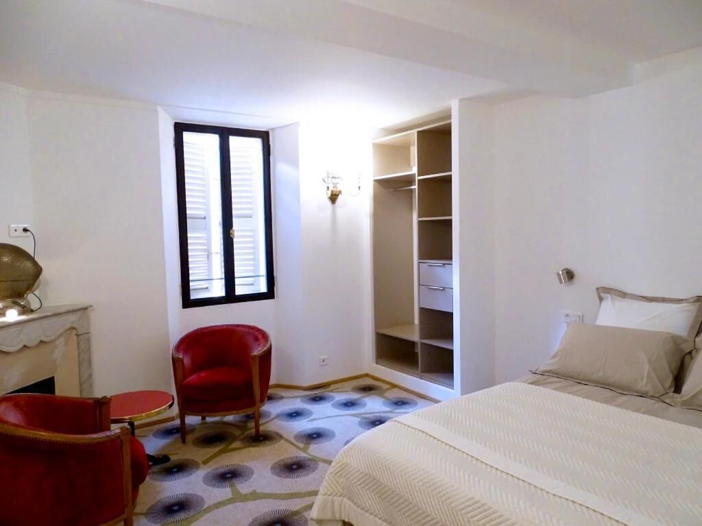 Una camera da letto con un letto, una sedia rossa, un tavolino, un armadio e una finestra.