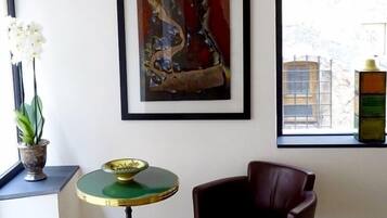 Habitació amb un sòl de fusta, una taula verd i daurada, una cadira de pell marró, un quadre abstracte emmarcat i una finestra amb vista a edificis.
