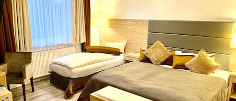 Habitación de hotel con cama, mesitas de noche, una silla, una mesa redonda con botellas y una ventana con cortinas.