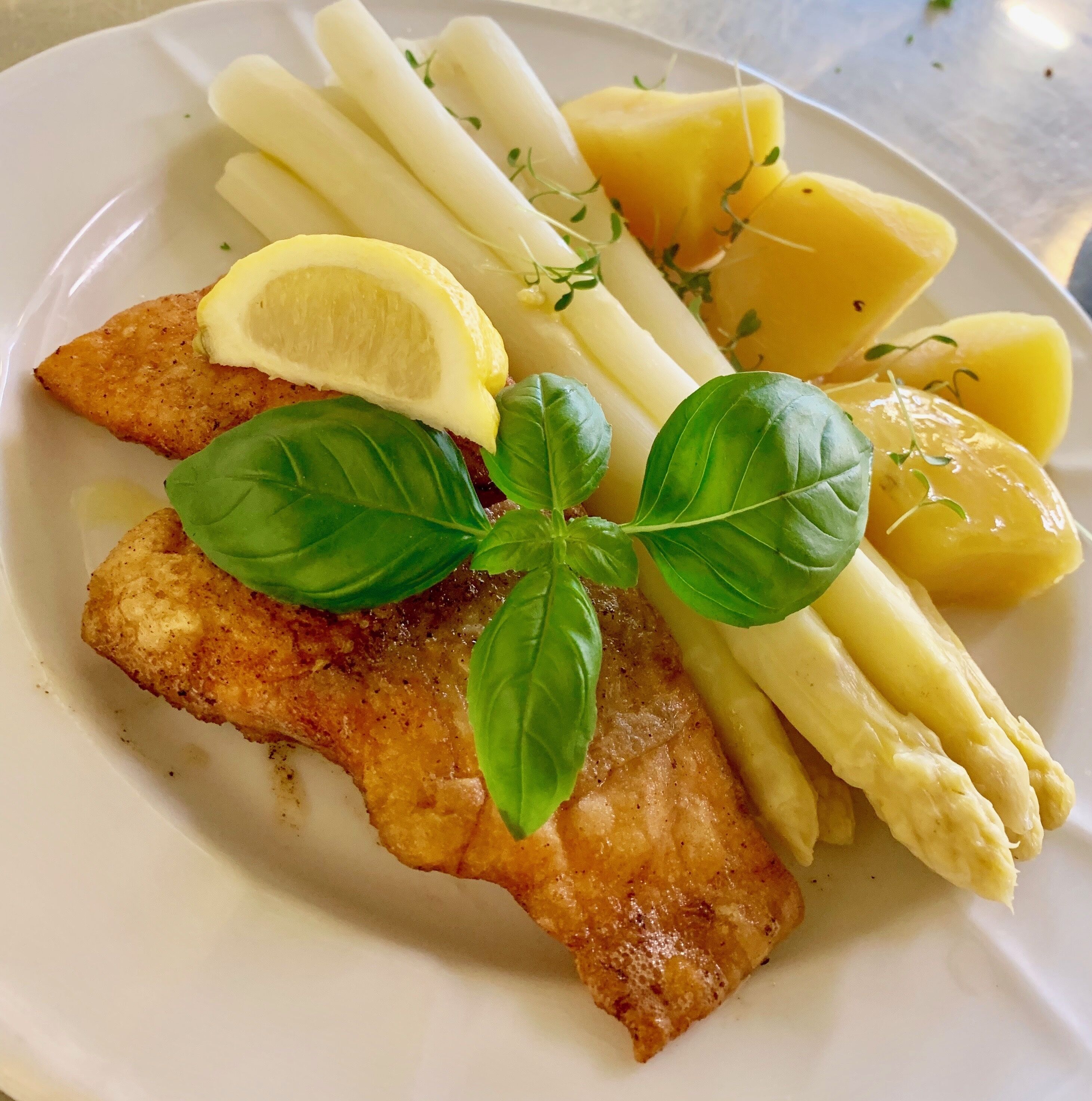 A plate with a breaded fish fillet, lemon wedge, asparagus, and potatoes.