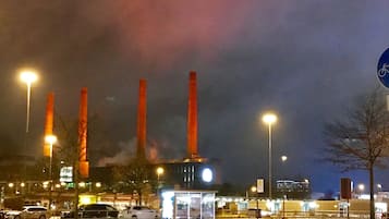 Nachtsicht auf eine Straße mit Bushaltestelle und einem Gebäude mit hohen Schornsteinen.