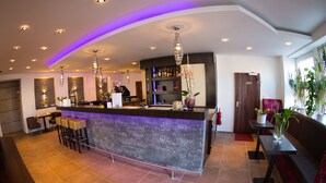 Zona de bar moderna amb un taulell corbat, tamborets i il·luminació penjant. Hi ha plantes en testos i una zona de seients amb un sofà i una taula.