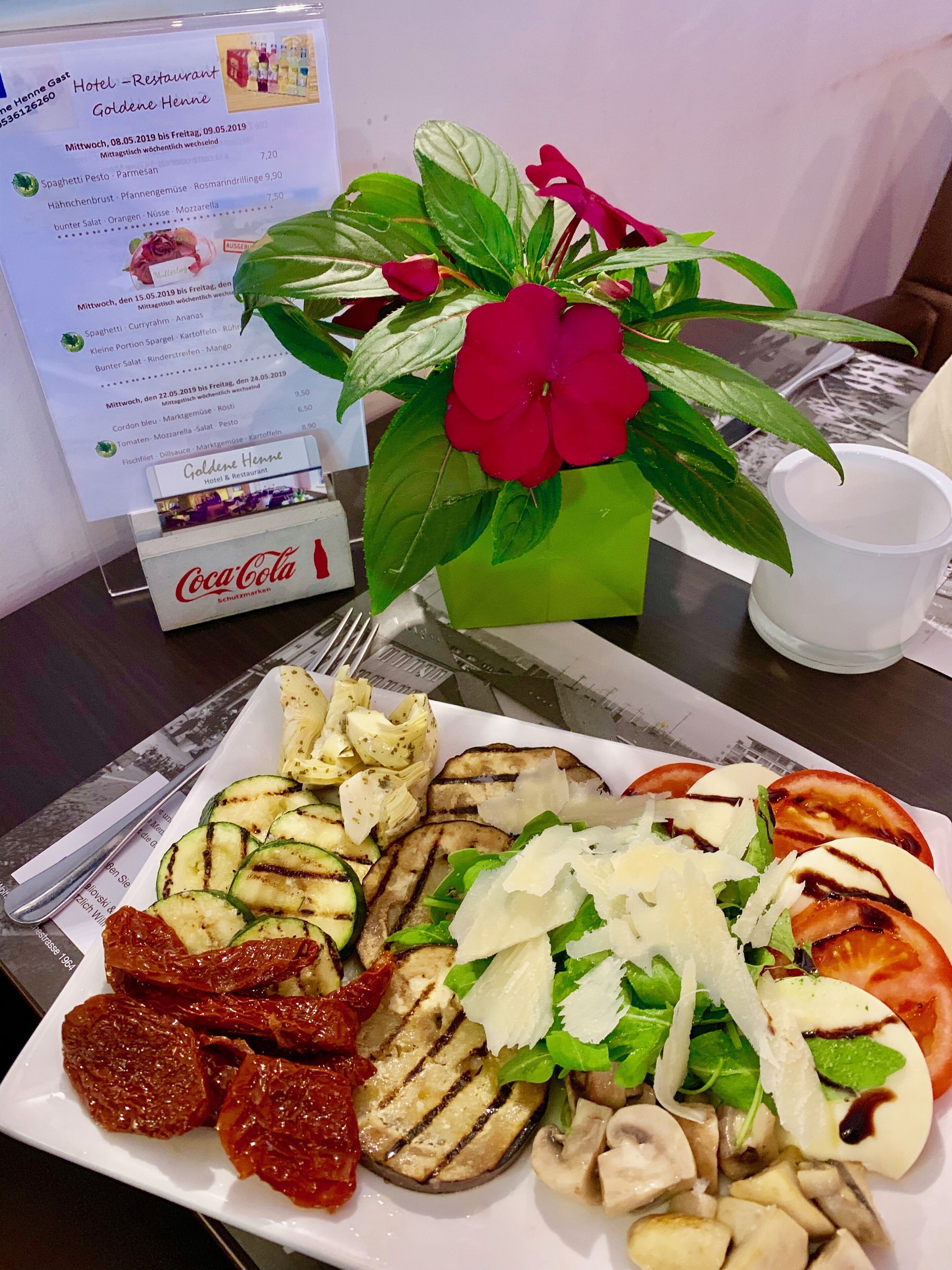 A meal with grilled vegetables and cheese, a Coca-Cola bottle, and a menu on a table.