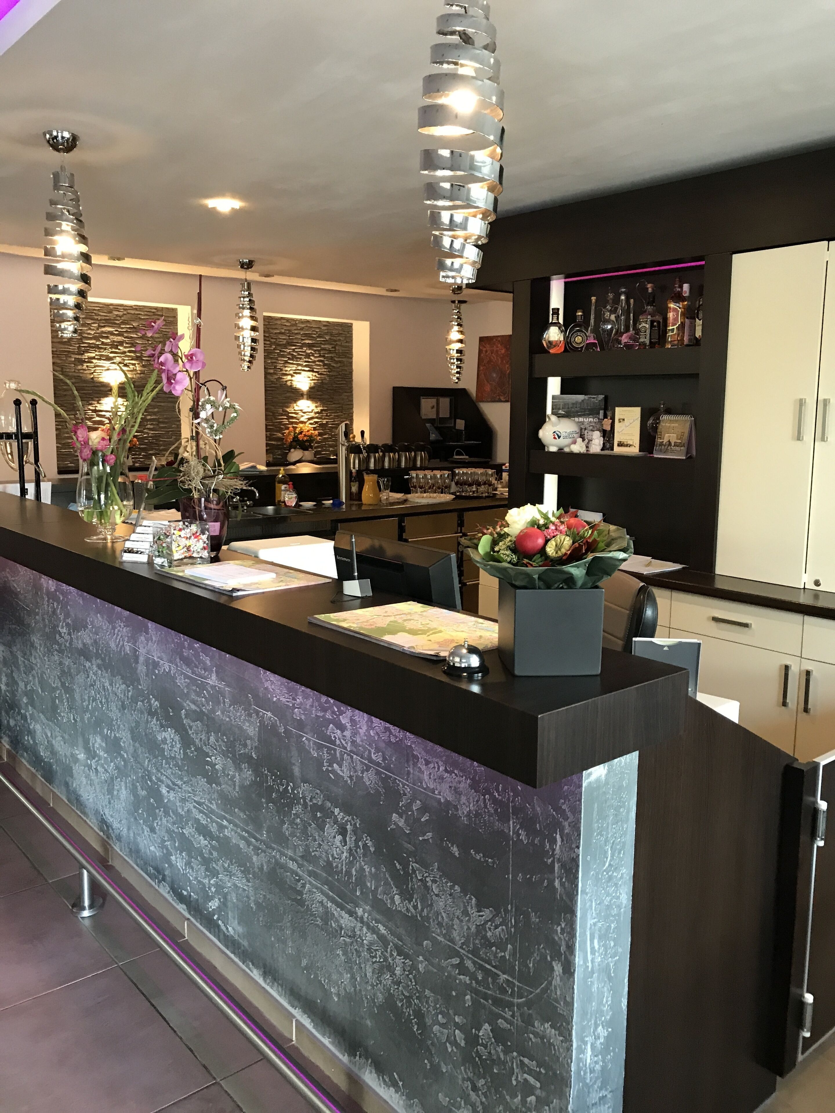 A modern reception area with a dark counter, decorative vases, and a bar area with bottles and glasses.
