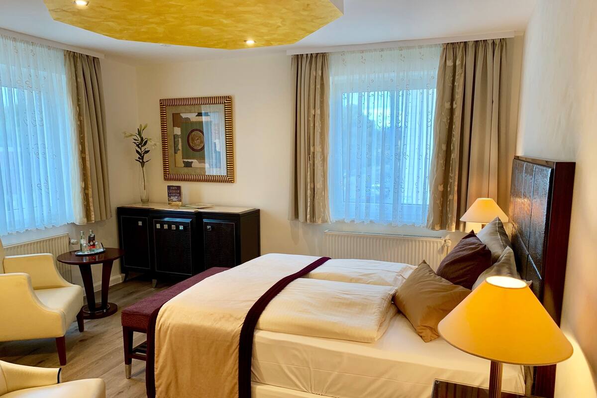 Una habitación de hotel con una cama grande, dos lámparas de noche, un escritorio con una computadora, una silla y un ventanal con cortinas.