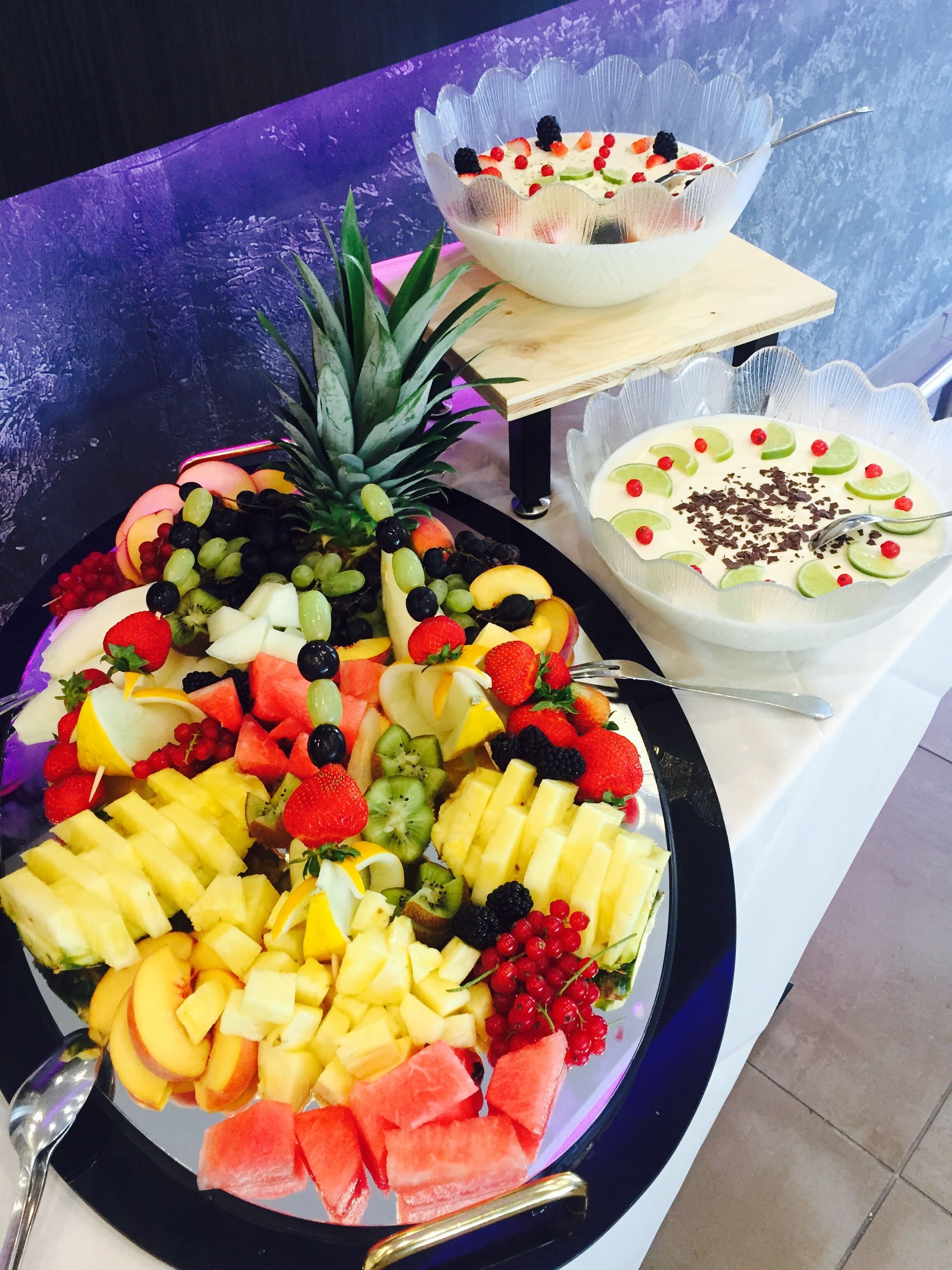 Una bandeja de frutas con diversas variedades y un bol de postre sobre una mesa.