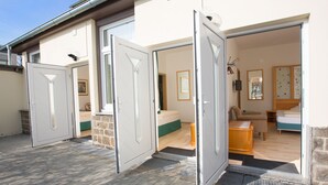 Una casa moderna amb tres portes obertes que donen a un saló amb un sofà, una taula petita i un llit.