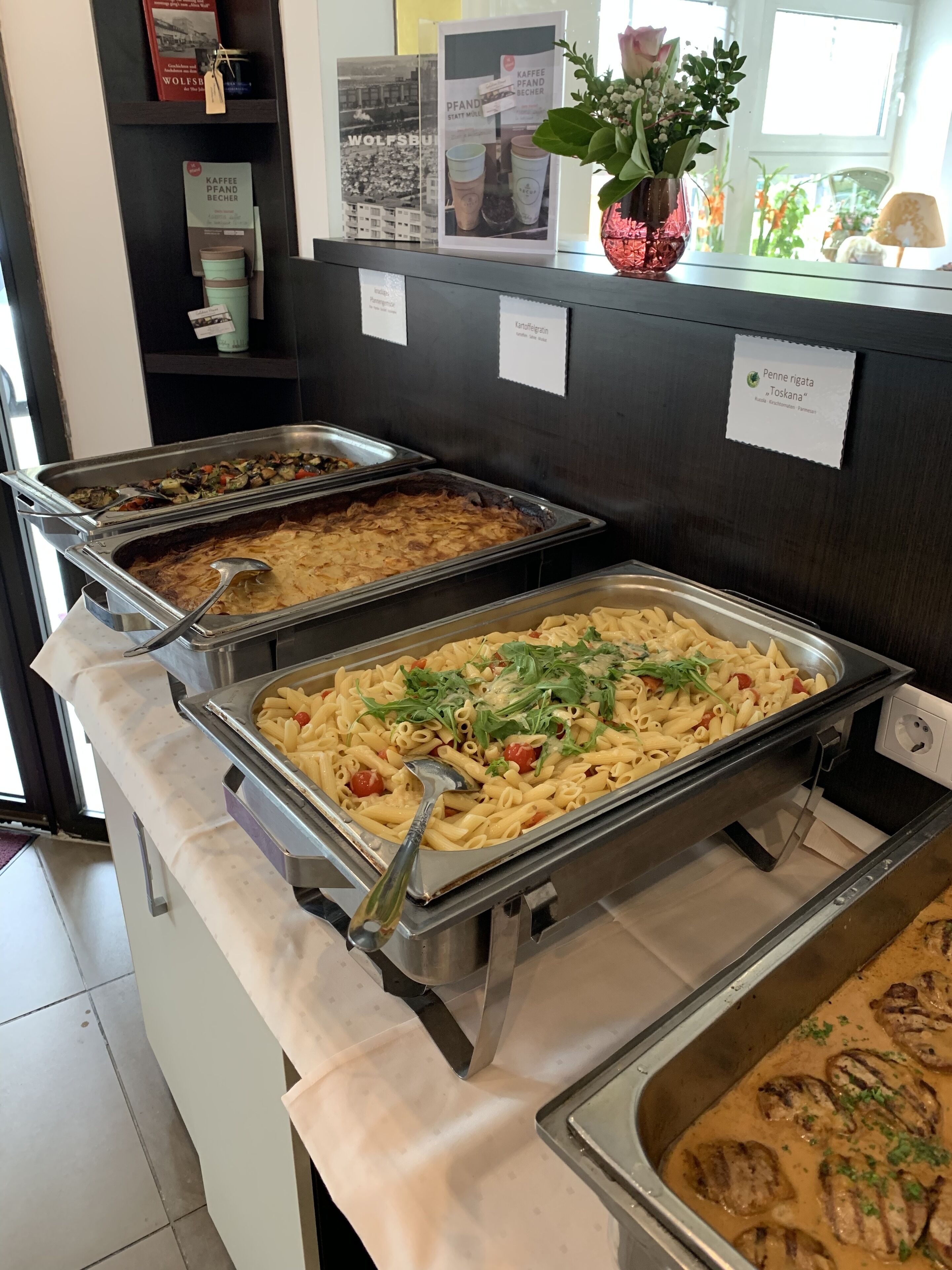 A buffet with various pasta dishes, a coffee station, and a flower arrangement.