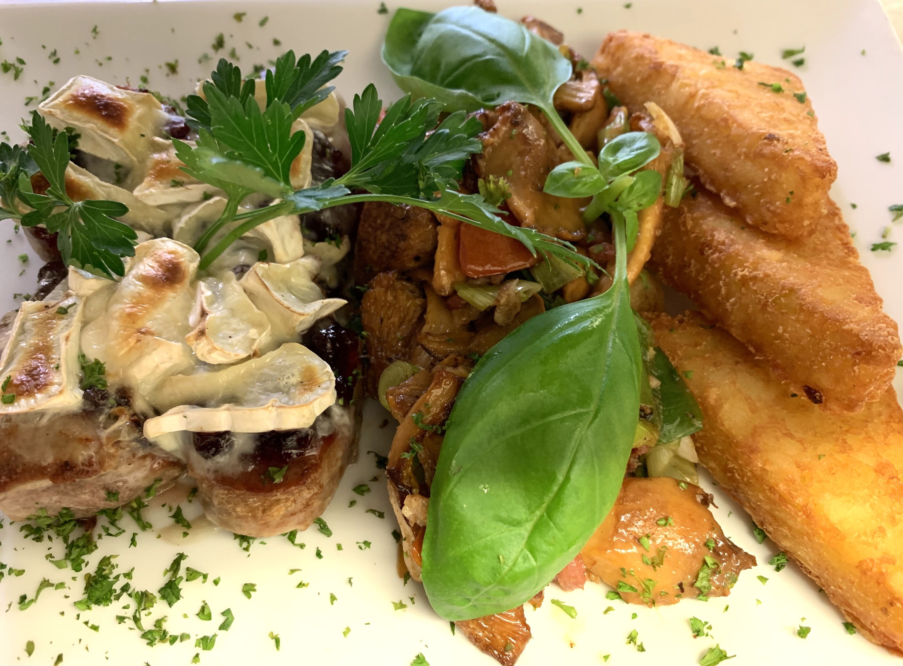 A plate of food with various items including a piece of meat, vegetables, and a leaf of basil.