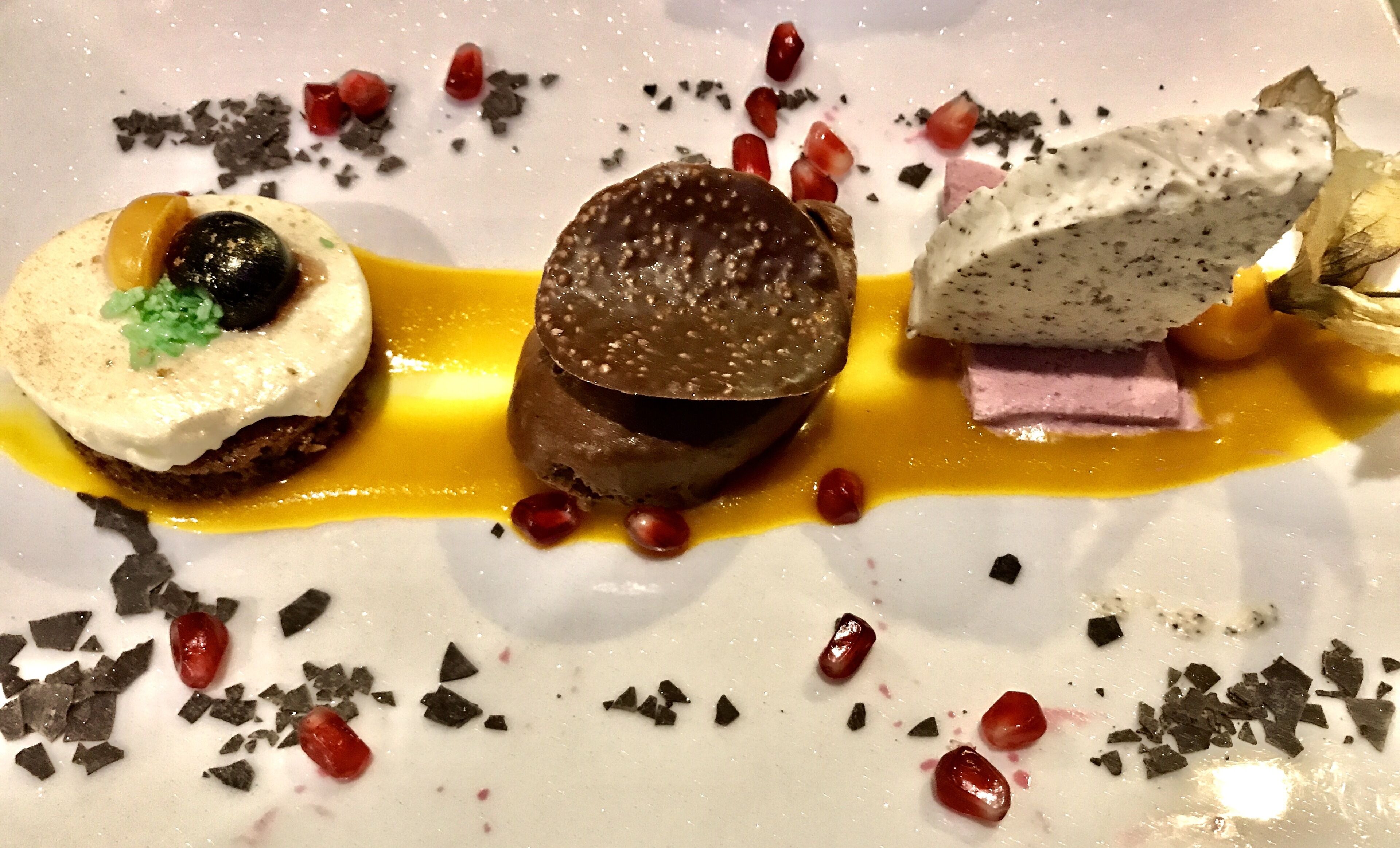 Um prato de sobremesa com três doces diferentes, decorado com raspas de chocolate e sementes de romã.
