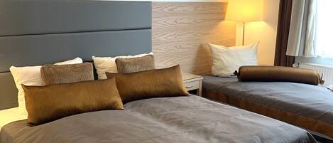 A hotel room with two beds, a bench, a lamp, and a window with curtains.