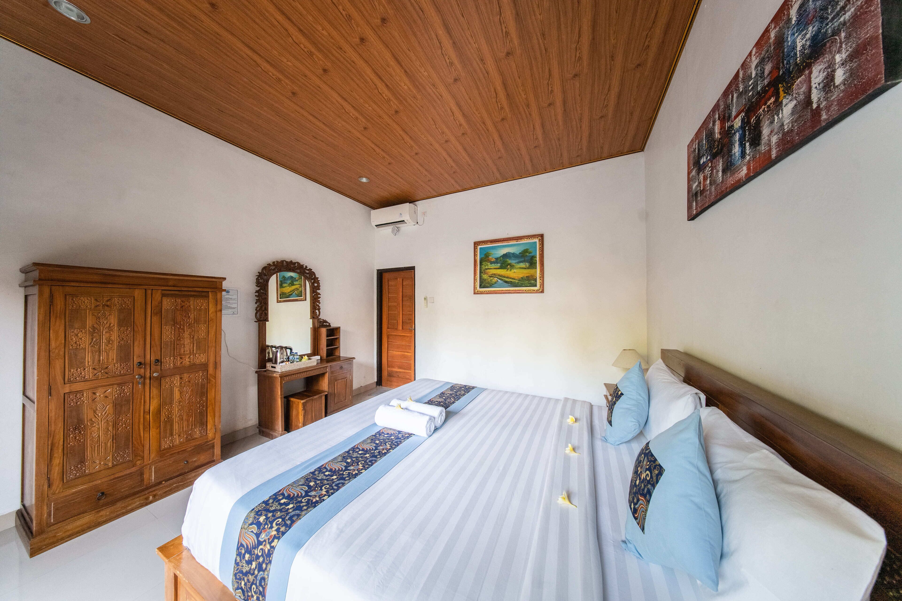 A bedroom with a large bed, wooden wardrobe, and a painting on the wall.
