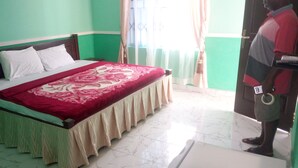 A room with a bed, green walls, a window with curtains, and a person standing by the door. - Great Mission Hotel (Oda)