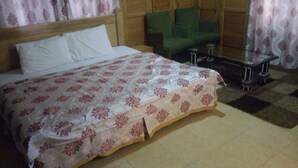 A hotel room with a bed, a green armchair, a small table, and a patterned bedspread. - Great Mission Hotel (Oda)