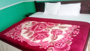A bed with a floral-patterned blanket, white pillows, and a green wall. - Great Mission Hotel (Oda)