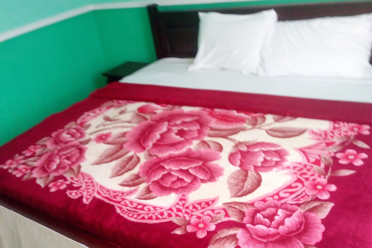A bed with a floral-patterned blanket, white pillows, and a green wall.
