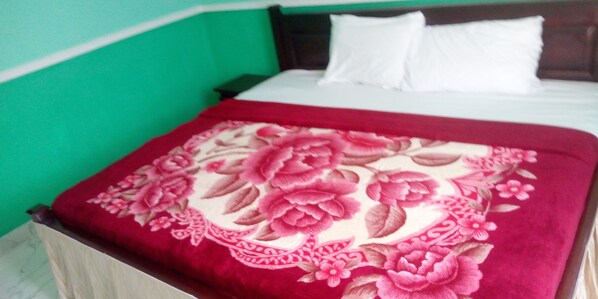 Una cama con una manta de estampado floral, almohadas blancas y una pared verde.