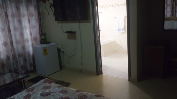 A room with a bed, a small table, a TV mounted on the wall, and a door leading to a balcony. - Great Mission Hotel (Oda)