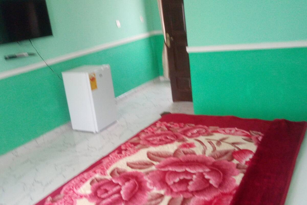 A room with a bed, a television mounted on the wall, and a small white appliance on the floor.