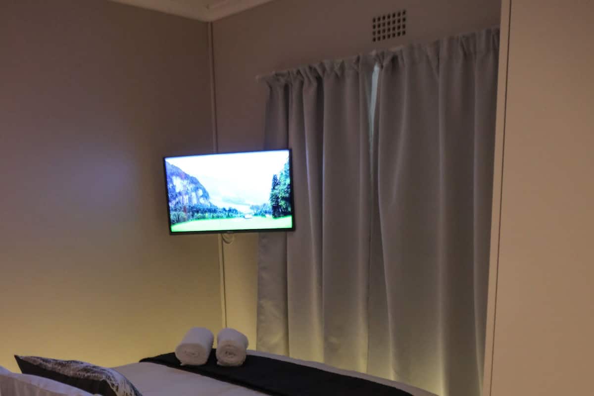 A hotel room with a bed, a flat-screen TV mounted on the wall, and a window with curtains.
