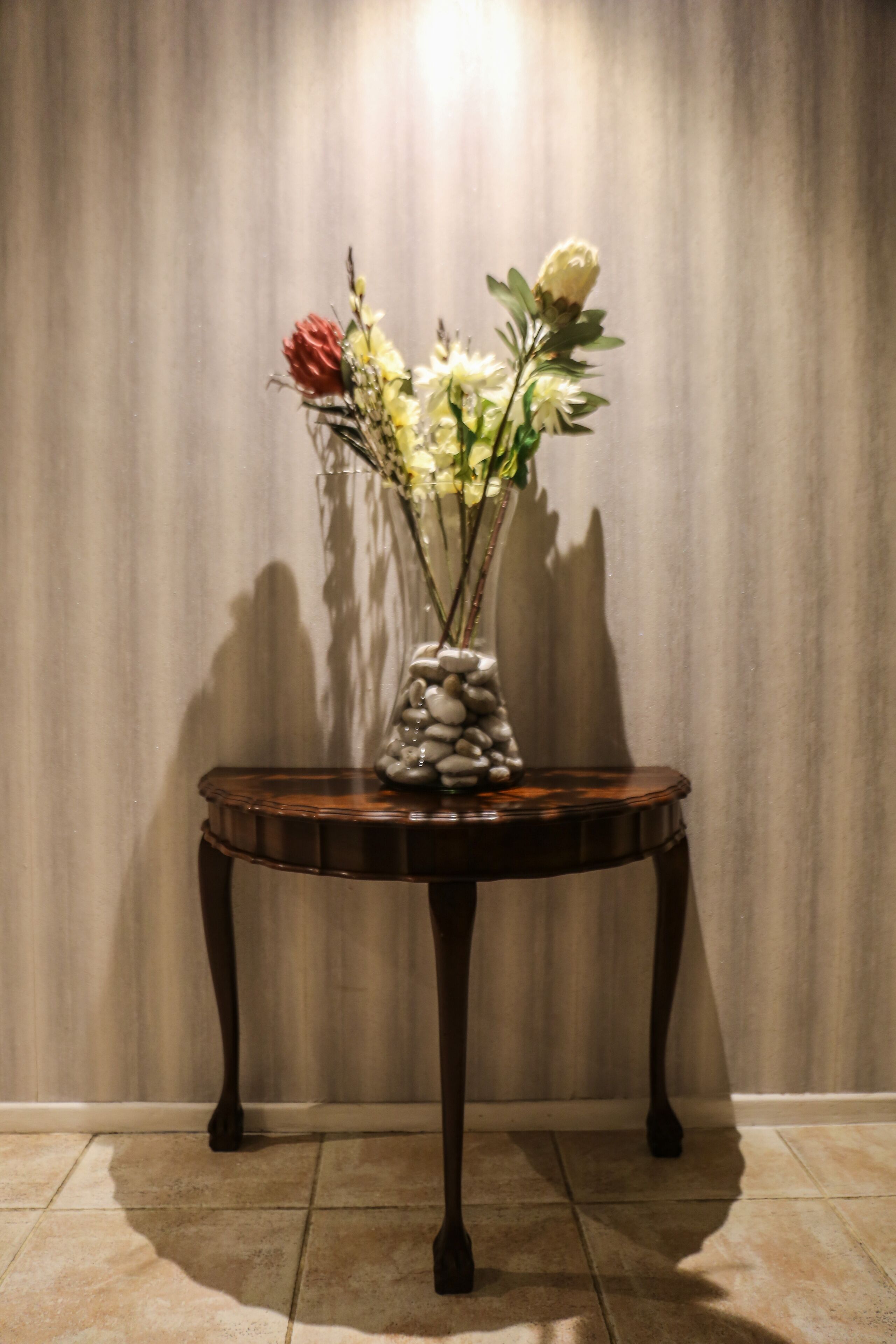 A table with a vase of flowers and a rock arrangement against a curtain backdrop.