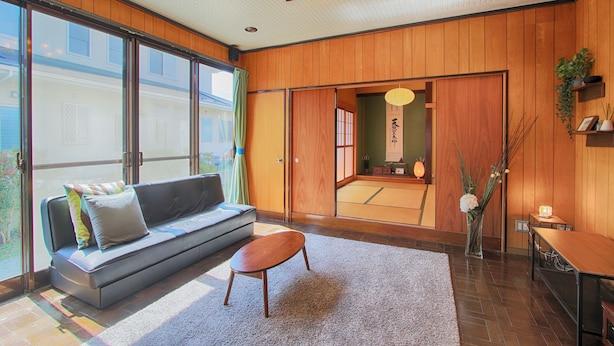 A modern interior with a sofa, a small table, and a view through large sliding doors. - Yoshimura House Hotel 6 (Fujikawaguchiko)