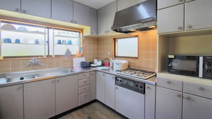 A kitchen with a sink, stove, and microwave. There are cabinets and a window above the sink. - Yoshimura House Hotel 6 (Fujikawaguchiko)