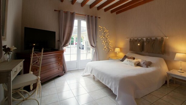 A bedroom with a large bed, a TV, a dresser, and a window with curtains. - Le Cabassou (Begadan)