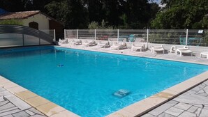 A swimming pool with a covered area, surrounded by white lounge chairs and a white fence. - Le Cabassou (Begadan)