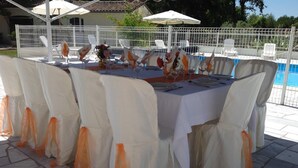 A table set for a formal outdoor event with white chairs and orange sashes, near a pool and white umbrellas. - Le Cabassou (Begadan)