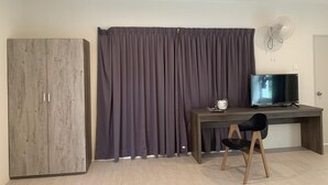 A room with a wooden wardrobe, a dark curtain, a desk with a chair, a television, and a wall-mounted fan. - The Sassy House (Langkawi)