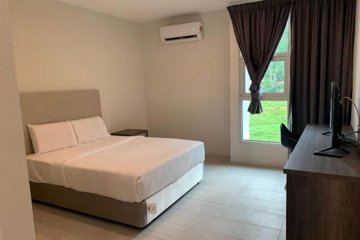 A bedroom with a bed, a desk, an air conditioner, and a window with curtains.