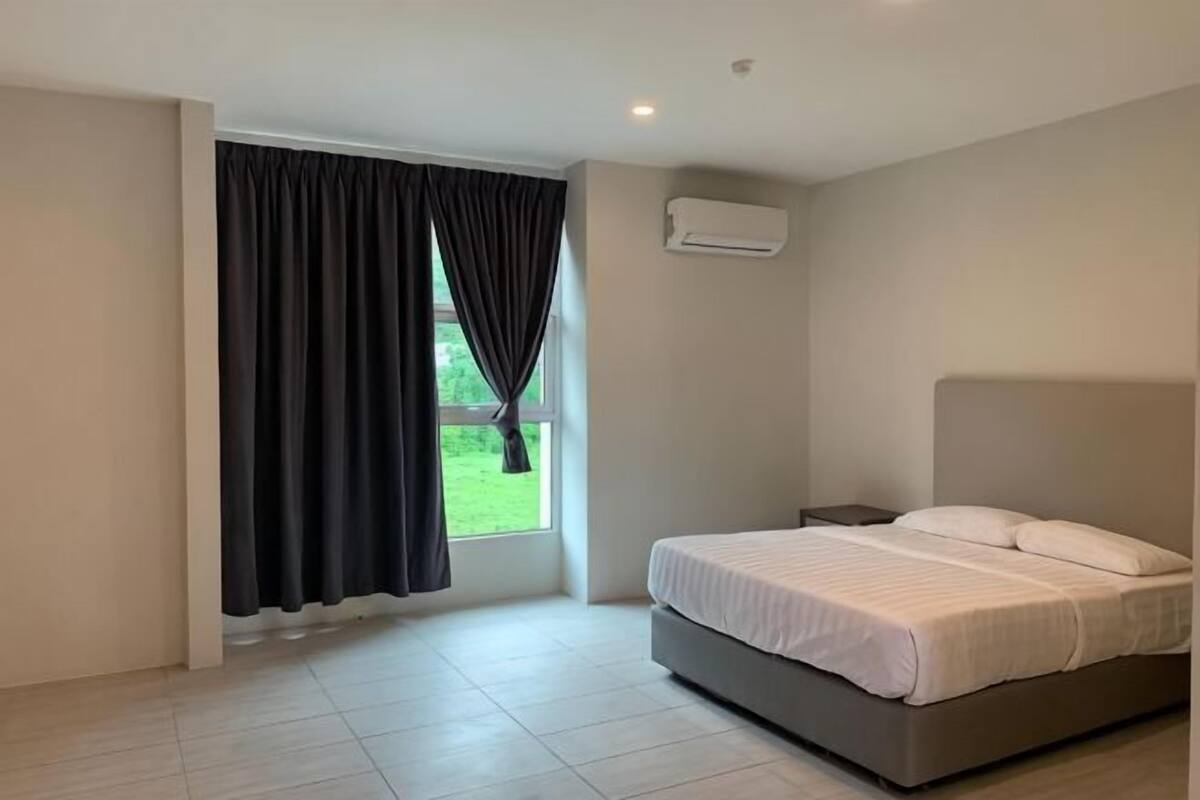 A bedroom with a bed, a window with curtains, a nightstand, and an air conditioning unit.