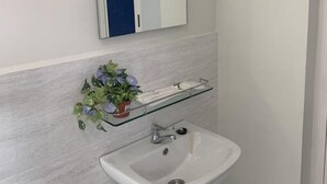 A bathroom with a white sink, a glass shelf with toiletries, and a mirror above it. - The Sassy House (Langkawi)
