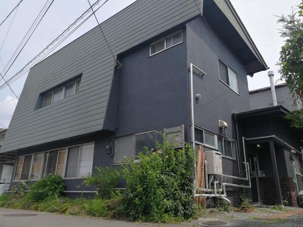 A two-story building with a dark exterior, a visible window, and some greenery in front.