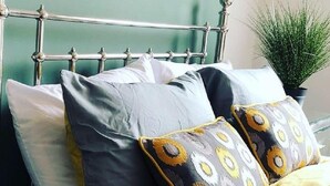 Una cama con cabecera de metal, ropa de cama gris y amarilla, y almohadas estampadas.