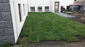 Ein Innenhof mit gepflegtem Rasen, einer Steinmauer und einer Tür, die zu einer Garage führt.