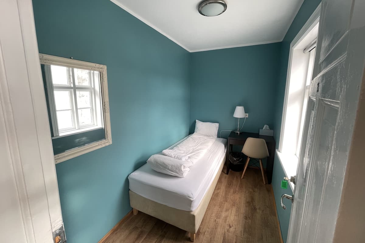 Une petite chambre à coucher, bien rangée, avec un lit simple, un bureau avec une chaise, une fenêtre et une porte.