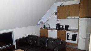 Ein kompakter Wohnbereich mit Küchenzeile, einem Ledersofa, einem Holztisch und einem Fernseher.