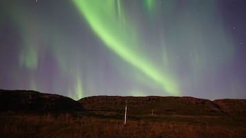 A night sky with the Northern Lights over a hilly landscape.