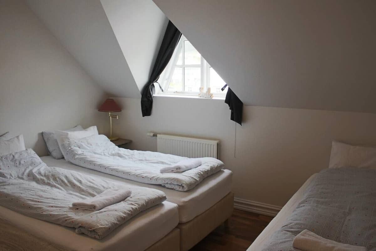 Une chambre avec deux lits, une fenêtre avec des rideaux, un radiateur et une lampe.