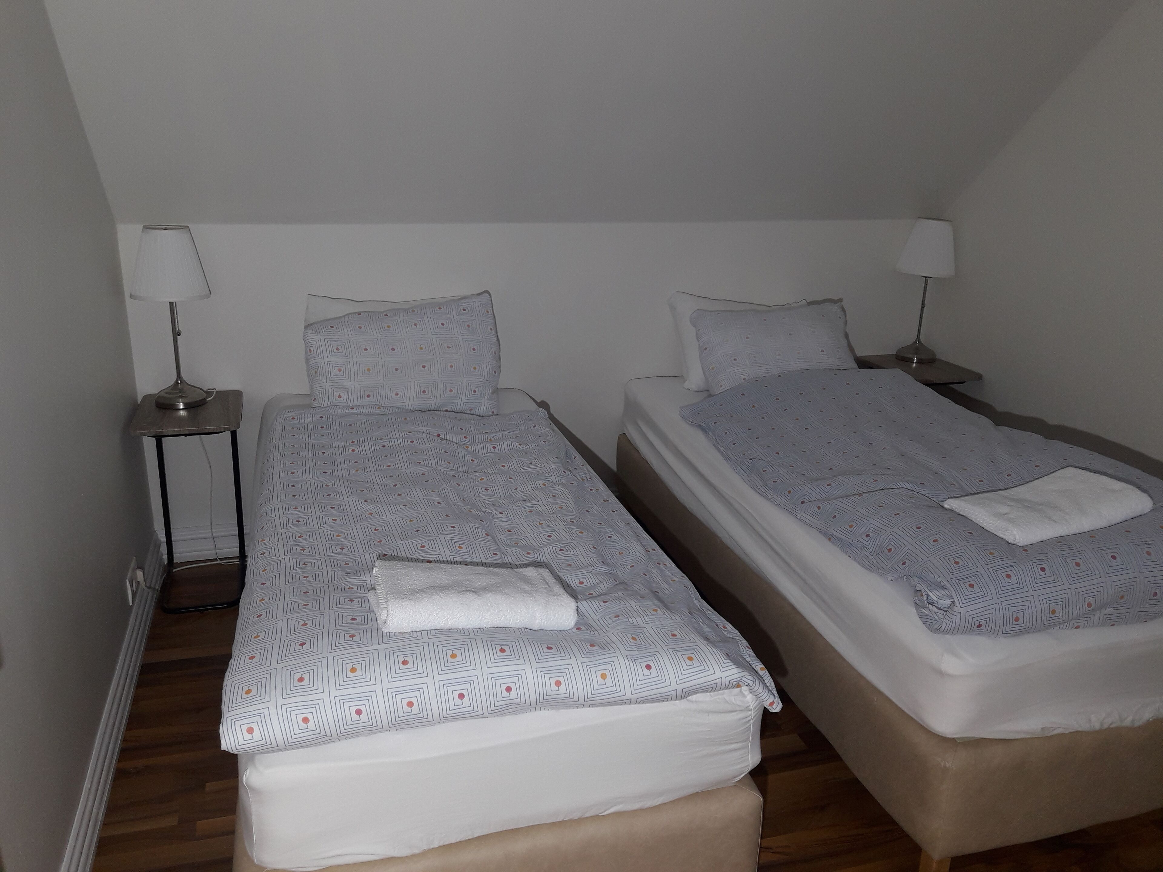 Habitación doble con dos camas individuales, cada una con almohada y lámpara de noche.