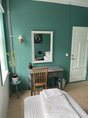 A room with teal walls, a white door, a desk with a chair, a bed with a white blanket, a potted plant, and a wall-mounted lamp. - Mánagisting Guesthouse (Isafjordur)