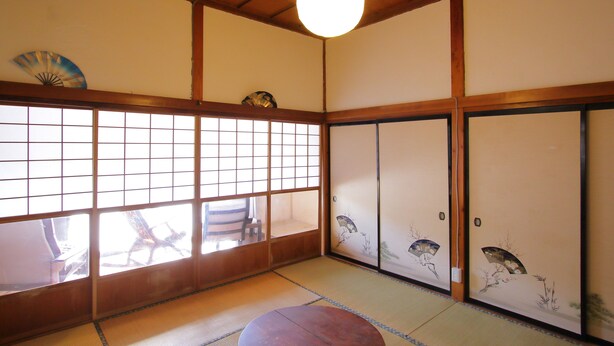 Une pièce de style japonais traditionnel, avec un sol recouvert de tatamis, des portes coulissantes décorées et un luminaire suspendu.