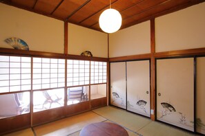 Ein traditioneller japanischer Raum mit Tatami-Böden, Schiebetüren mit Kunstwerken und einer hängenden Leuchte.