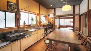 Une cuisine de style japonais traditionnel, avec des meubles en bois, une cuisinière à gaz et un coin repas comprenant une longue table en bois et des chaises.