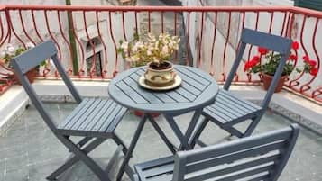 A balcony with a table and chairs, a potted plant, and a view of the street.