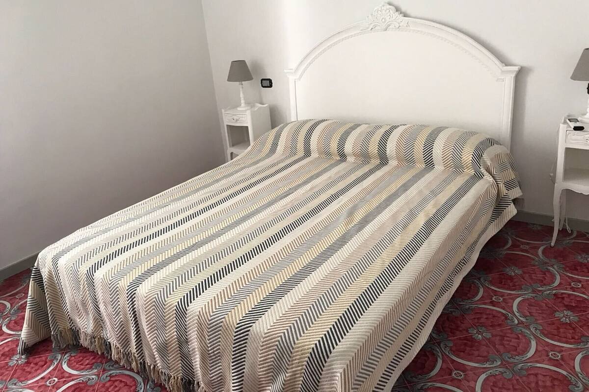 A bed with a patterned bedspread, white headboard, and two bedside tables with lamps.