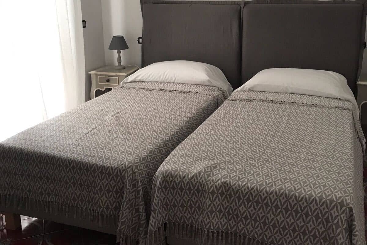 A double bed with patterned bedding, a bedside table with a lamp, and a window with curtains.